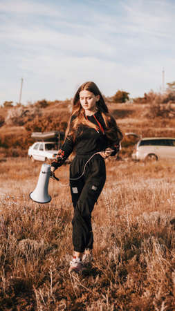 Girl in black goes through meadow with megaphoneの写真素材