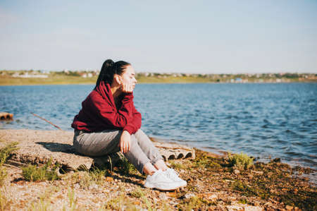 Cute girl sits near the river with closed eyesの写真素材