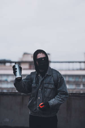 Anonymous in mask and glasses checks spray paint can on the roofの写真素材