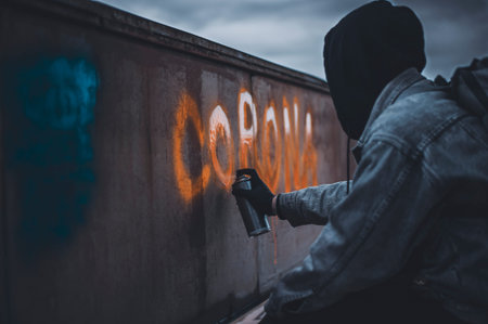 Man in black hood paint corona lettering with orange spray paint