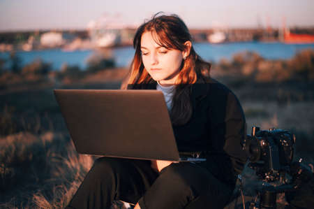 Pretty girl with laptop and camera on a hillsの写真素材