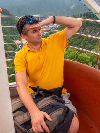 Adult man on ropeway looks on a mountains aroundの写真素材