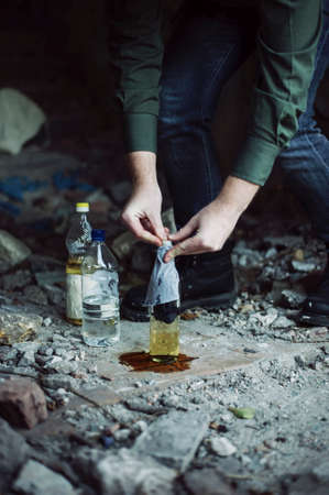 Man in military clothes makes a molotovs cocktail in time of city protestsの写真素材
