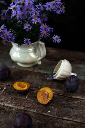 Delicate blue flowers in white vase near orange plumの写真素材