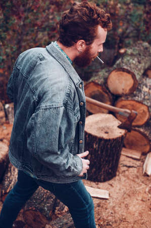 Brutal redhead guy with cigarette gets ready to chop woodの写真素材