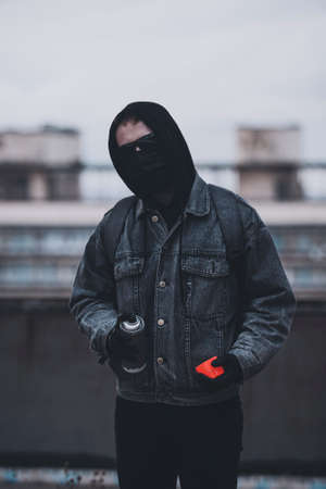 Punk with red spray can hide his identity with mask and hood in time of political protestの写真素材