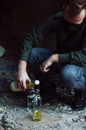 Young soldier mix ingredients to make molotov cocktail. Deserted urban atmosphere.の写真素材