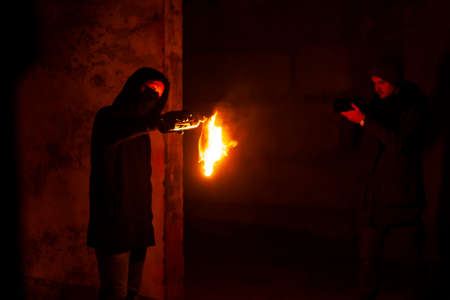 Man in hood and mask takes flaming molotovs cocktail while cameraman shoots it on cameraの写真素材