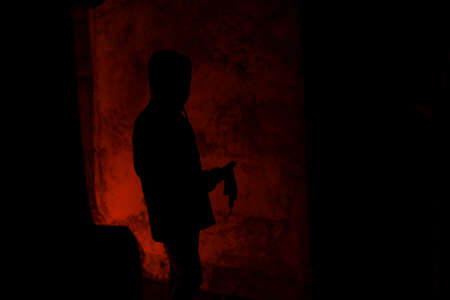 Silhouette of man taking molotovs cocktail in hood on the flame light on wall backgroundの写真素材