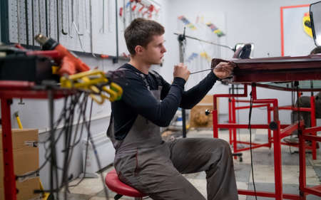 Dent removing work process of young professional car repair employer. He uses innovative paint less methodic.の写真素材