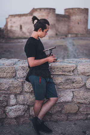 Pretty young pilot with long hair looks on the remote control near old wall. Medieval castle on the backgroundの写真素材