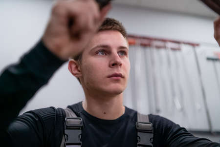 Concentrated blue eyes sight of young repair specialist leveling harmed car detail using rubber hammer intently aim movingの写真素材