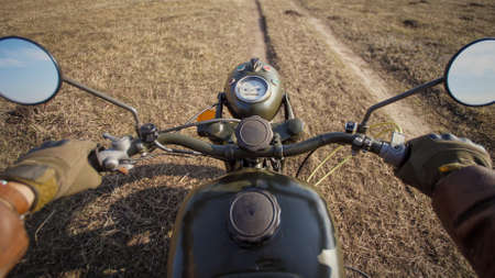 POV biking dirt road through wild autumn valley on vintage motorcycle military styled. Dangerous cross country riding.の写真素材