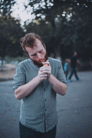 Bearded man in checker shirt lights up weed in public place. Addiction in public parkの写真素材