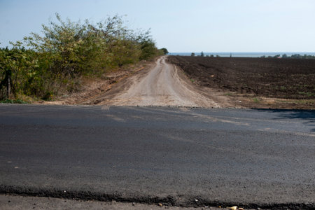 View of the half-asphalt crossroad on the field near the sea. A symbol of unequal developmentの写真素材