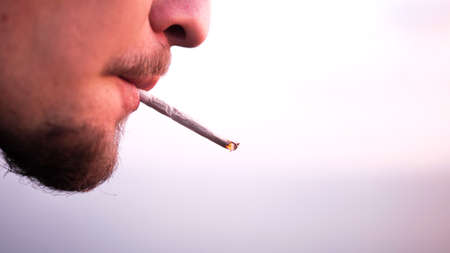 Close-up shot in profile of man who smokes cigarette in sunny day and makes a firsts puffs.の写真素材
