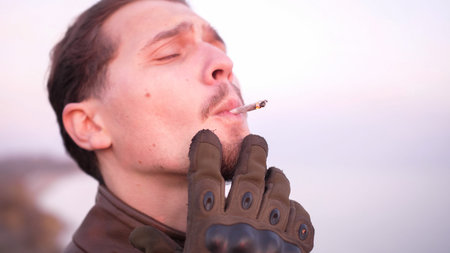 Emotional portrait of a curly handsome man enjoy a hand rolling marijuana joint. He close his eyes...