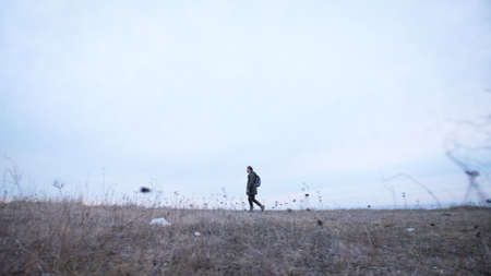 Curly guy in trekking clothes with backpack lonely walks a desert hills in late autumn side view He goes along the edgeの写真素材