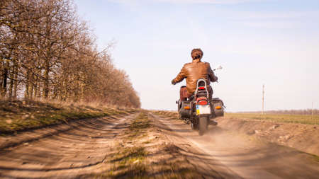Guy in leather jacket riding through the fields off-road countryside on chopper in autumn sunny day,の写真素材