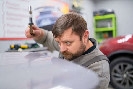 Close shot of dent removing without paint, bearded professional worker makes accurate blow rubber hammerの写真素材