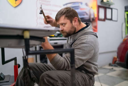 Close shot of dent removing without paint, bearded professional worker makes accurate blow rubber hammerの写真素材