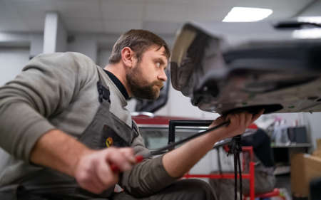 Bearded mans car repair service worker, hands photo in work repair process with a car doorの写真素材