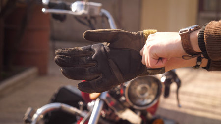 Photo of a bikers hands in gold hours wear protection gloves with a red chopper on background.の写真素材