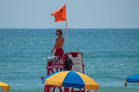 Daytona Beach Florida. July 07, 2019 Top view of lifeguard in red tower and colorful umbrella.のeditorial素材