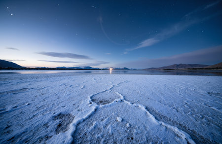 Frozen lake at night with starry sky and mountains in the backgroundの素材