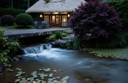 Japanese garden with a small waterfall and a wooden house in the backgroundの素材