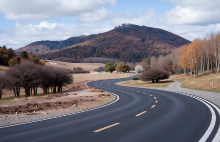 Asphalt road in the autumn forest with mountain view and blue skyの素材