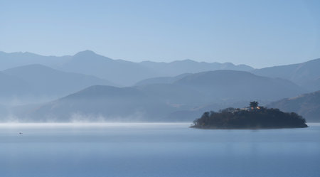 Island in the sea with fog and mountains in the background.の素材