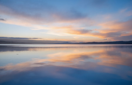 Reflection of clouds in the calm water of a lake at sunsetの素材