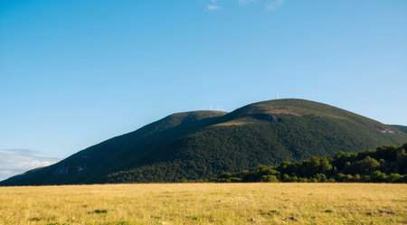 Mountain landscape with green grass and blue sky with white clouds.の素材