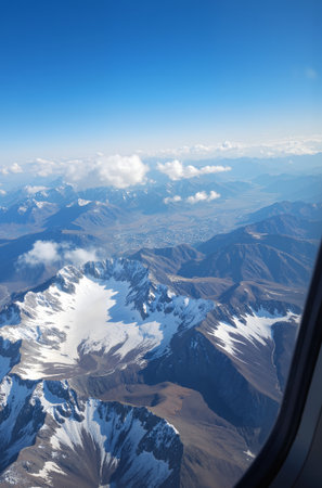 Aerial view of snow capped mountains and blue sky from airplane windowの素材