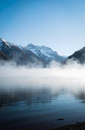 Mountain lake in the morning mist with snow and clear blue skyの素材