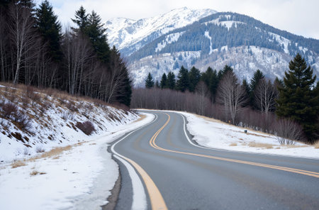 Winding road in winter landscape with snow covered mountains in the backgroundの素材