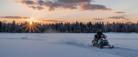 A man on a snowmobile rides through the winter forest at sunset.の素材