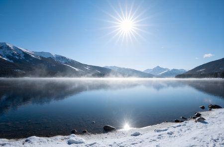 Beautiful winter landscape with snow covered mountains and lake under blue skyの素材