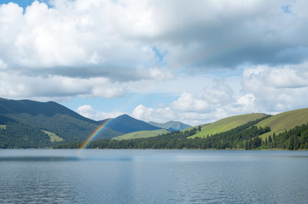 Rainbow over a lake in the mountains under a cloudy sky.の素材