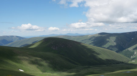 Mountain landscape with grassland, blue sky and white clouds.の素材