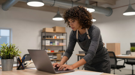 Portrait of a young man in an apron working on a laptop in an officeの素材