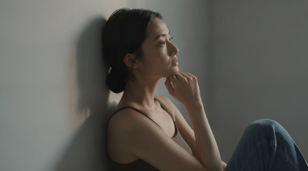 young beautiful sad and depressed Asian Korean woman sitting alone at home living room floor looking desperate suffering depression problem and anxiety crisis in social problemの素材