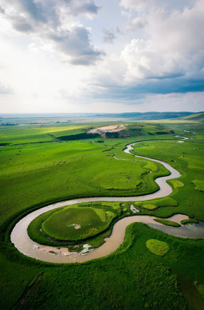 Aerial view of small river flowing through green grassland at sunsetの素材