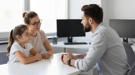 Young father and daughter sitting at desk in office, looking at each other, talking to each other. Father and daughter sitting at table, discussing business issues. Teamwork conceptの素材