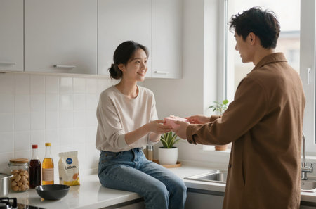 Young asian couple holding hands and smiling while sitting in kitchen at homeの素材