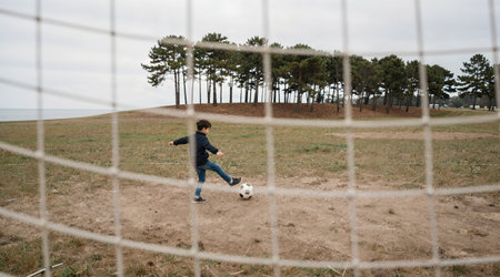 Young boy playing football on a beach in autumn, wearing a jacketの素材
