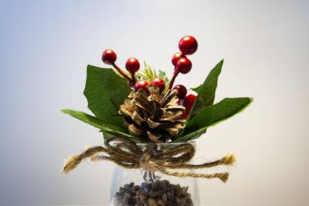 In a glass vase there are artificial berries, leaves, and a cone.の写真素材