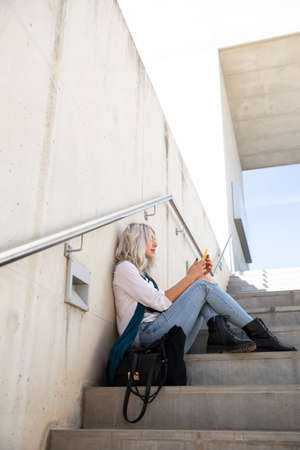 a confident professional young blonde woman using a smartphone outdoorsの写真素材