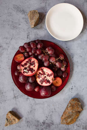 still life raw plums, pomegranate and grapes in a grey stone backgroundの写真素材